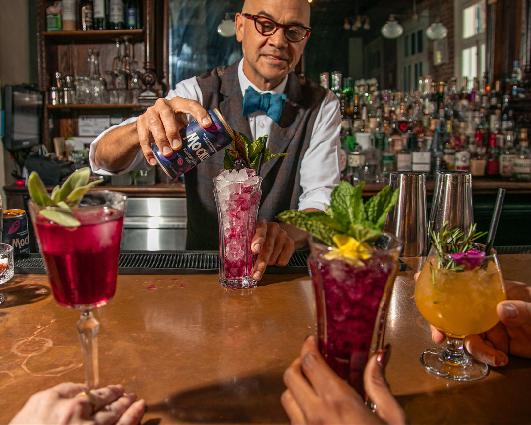 Bartender preparing cocktails at a bar with patrons holding drinks.