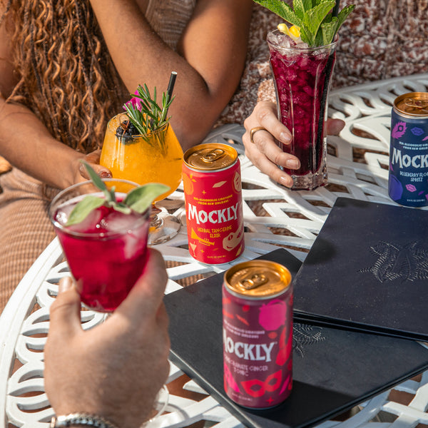 Two people sitting at a table with Mockly drinks and cans.